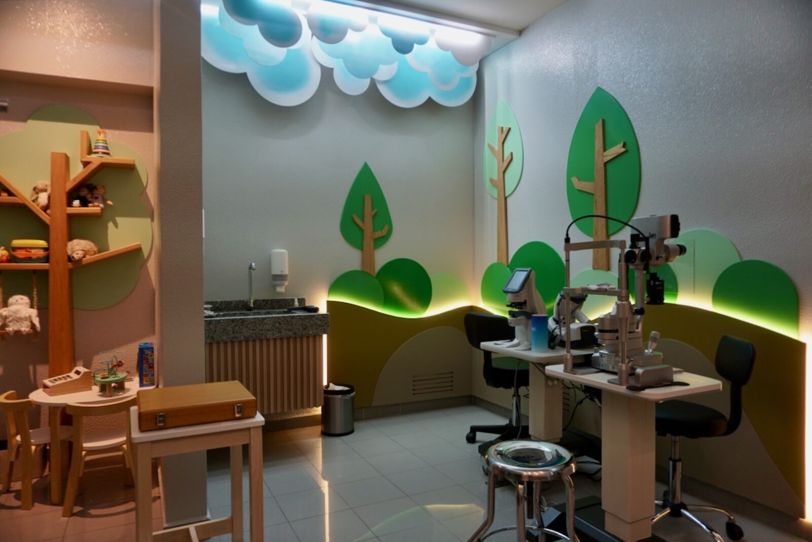 Play corner with a tree bookshelf of plush toys next to the eye examination station